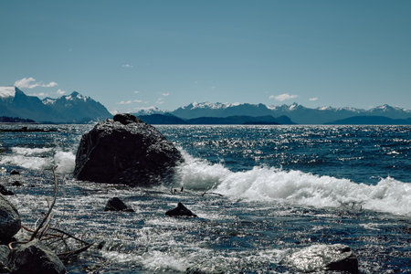 Picturesque rocky mountains in a turquoise lake. Waves foam around a huge stone. Clouds in a clear blue sky.の写真素材