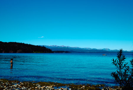 Beautiful mountain lake. Transparent blue water. Surrounded by rocky mountains and forest. A boat in the distance with swimmers.の写真素材