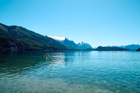 Beautiful mountain lake. Transparent blue water. Surrounded by rocky mountains and forest. A boat in the distance with swimmers.の写真素材