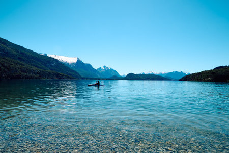 Beautiful mountain lake. Transparent blue water. Surrounded by rocky mountains and forest. A boat in the distance with swimmers.の写真素材