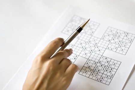 A hand holding a mechanical pen on a sudoku grid.の写真素材