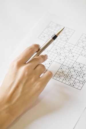 A hand holding a mechanical pen on a sudoku grid.の写真素材