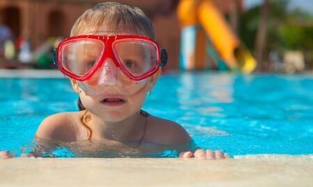 Little girl in a mask for diving on the edge of the poolの写真素材