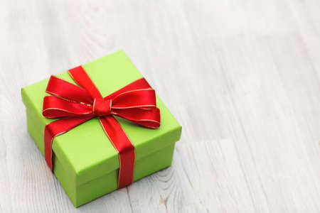 Green gift box with red ribbon bow laid on a wooden background. Top view Christmas background