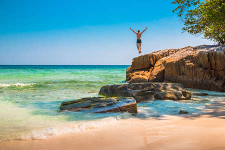 The happy young man jumping off cliff into the ocean. Summer fun, lifestyle, extreme sport.の写真素材
