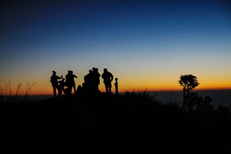 Silhouette picture of Tourists stand on the mountain at dawn to see the sunrise in the background.