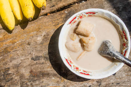 Banana in coconut milk dessert is placed on the old wooden table background.の写真素材