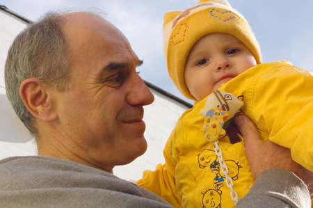 Grandfather holds his granddaughter in hands against the blue skyの写真素材