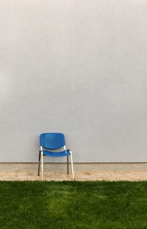 blue chair next to gray wall and green grass, copy spaceの写真素材