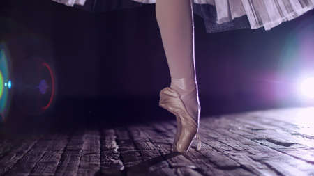 close up, in rays of spotlight, on stage of old theater hall. ballerina in white ballet skirt, rotates on toe in pointe shoe, performs elegantly a certain ballet exercise, tour,pointe. High quality photoの写真素材