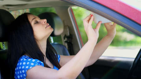 beautiful brunette woman sitting in the car, looking in the mirror, straightening up the hairstyle and apply make up. summer. High quality photoの写真素材