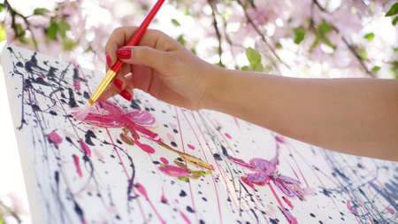 close-up, female hand, painter, artist paints a picture of flowers in blooming spring apple orchard, she applies oil paints to canvas with brush, creative process. High quality photoの写真素材