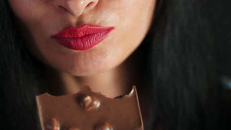 Sweet temptation. Cropped closeup of a red lipped female biting on a chocolate, Lips of beautiful sexy brunette woman eating chocolate with hazelnuts. High quality photoの写真素材