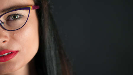 portrait of a sexy brunette woman with red lips who eroticly and playfully tries on stylish glasses, spectacles and looking sexually at camera in studio. dark gray background. High quality photoの写真素材