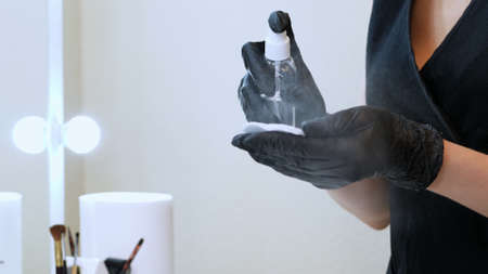 beauty saloon. close-up, the master in black special gloves holds a cotton pad and sprinkles it with...