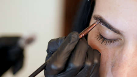 close up. young woman gets eyebrow correction procedure. kosmetolog- makeup artist applies paint...