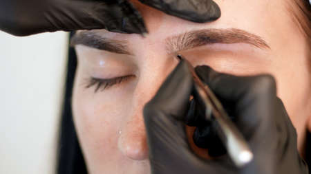 beauty saloon. close-up, hands of the cosmetician in black rubber gloves hold tweezers and pull out eyebrows. Master corrects the shape of the eyebrows. High quality photoの写真素材