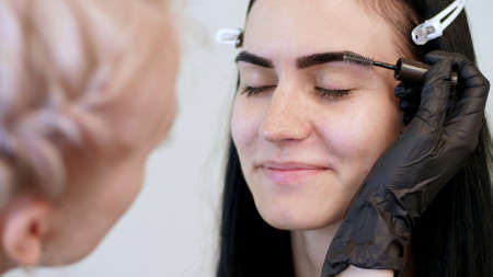 beauty saloon. close-up, a beautician in black rubber gloves, gently combs the eyebrows of the...