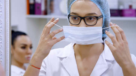 cosmetology room in the clinic, a female doctor wearing glasses, wearing a white uniform, dresses a...