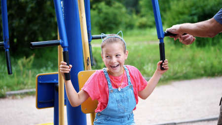 smiling, happy eight year old girl engaged, doing exercises on outdoor exercise equipment, outdoors,...
