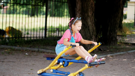 smiling, happy eight year old girl engaged, doing exercises on outdoor exercise equipment, outdoors,...