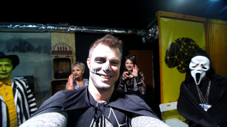 Halloween party, night, frightening portrait of a man with a terrible makeup in a black witch suit, croaks in front of the camera, in the background Halloween scenery is seen. High quality photoの写真素材