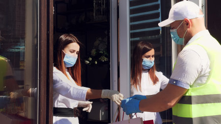 delivery service for parcels, gifts. courier wears protective mask. designer, in mask, gives him a...