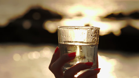 glass of water at sunset. close-up. silhouette of a female hand holds a glass with clear water....