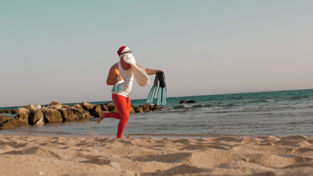 Santa Claus summer vacation. Santa Claus having fun. Funny Santa, in sunglasses, with flippers and snorkeling mask, runs along sea beach. He is in a hurry to swim, snorkel. High quality photoの写真素材