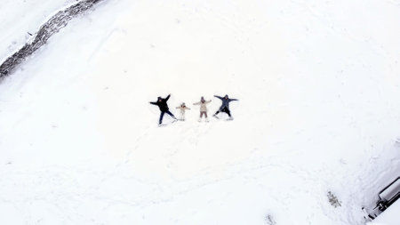 winter family fun. Happy family of 4 are making angels on the snow. aero, top view. Family is enjoying of snow and snowfall, having fun on snowy winter day, outdoors. High quality photoの写真素材