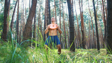 Young athletic man, with a bare, naked torso, performs strength exercises with heavy weight plate,...