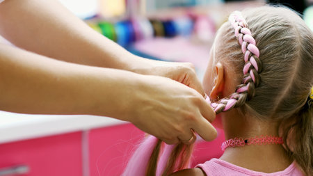 Beautiful blond girl, of seven years old, braided two pigtails, do a hairstyle with pink locks of...