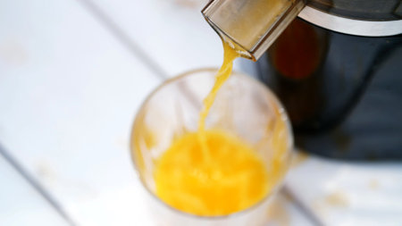 close-up, from the juicer flows freshly squeezed orange juice into a glass. view from above. High...