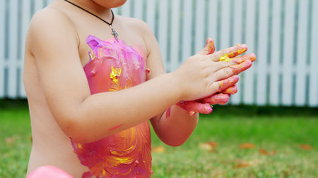 a little child, a four-year-old boy playing, painting with finger paints, decorating himself, in the garden, sitting on a blanket, on grass, lawn, in the summer. hes having fun. High quality photoの写真素材