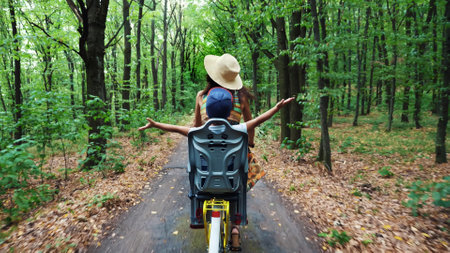 a woman in a hat and dress, with a basket of flowers, together with small child, ride bicycle, in the forest, in the summer. the child is sitting in a special chair. High quality photoの写真素材