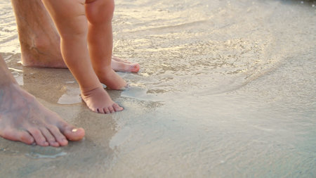 close-up, on wet sand, there are male and childrens feet. a wave comes in. Vacation on ocean beach, Summer holiday. High quality photoの写真素材