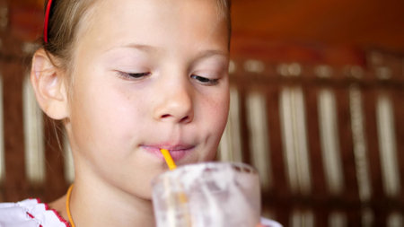 happy smiling teen girl child drinks a milkshake in cafe. she is dressed in Ukrainian national clothes, embroidery, vishivanka. High quality photoの写真素材