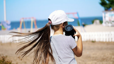 back view, teenage child, long-haired blonde girl in a blazer listening to music with portable speaker , on the beach, dancing , on a hot summer day. High quality photoの写真素材