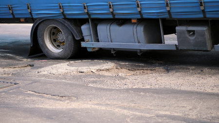 close-up, very poor road coverage, many pits, curved asphalt, a large truck slowly passes a stretch of road in disrepair. the road needs repair. High quality photoの写真素材