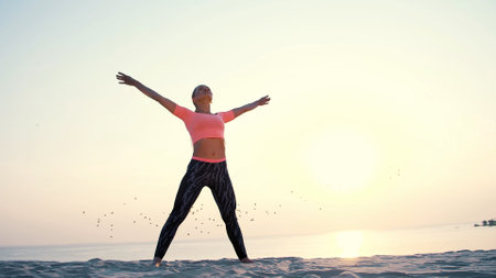 Healthy, young beautiful woman meditating, stretching, practicing yoga on the sea beach, at sunrise,...