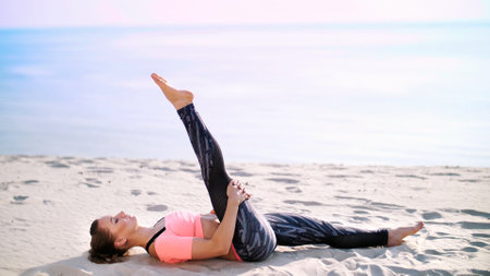 Healthy, young beautiful woman performs exercises for muscles of the press, picks up the body, legs, pumps the press lying on the sand, on the beach, at sunrise. High quality photoの写真素材