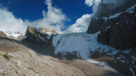 Aksay Glacier in Kyrgyz Mountains with rocks, snow, Ice, and clouds on dark blue skyの写真素材