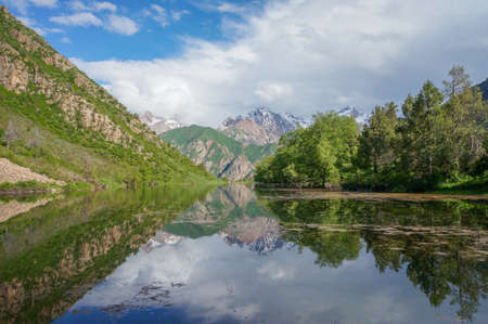 An amazing lake reflecting the white peaks of the mountains and green vegetationの写真素材