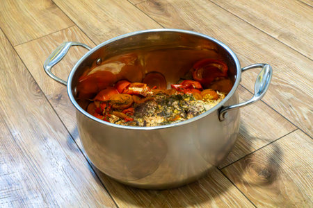A large stainless steel pot filled with cooked crab and vegetables on a wooden floor, representing...