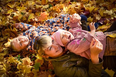 Family of mother and two kids relaxing on bright autumn leaves