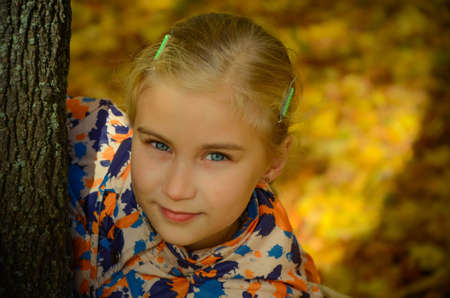 Pretty girl looking out from behind a tree in autumn parkの写真素材