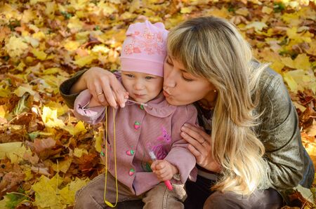 Young woman playing with  her little daughter in the bright autumn parkの写真素材