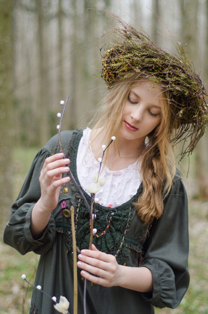 Portrait of a girl in a folk  medieval style with a circlet of flowers looking at the willow branchの写真素材