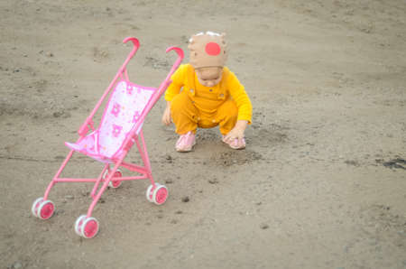 Photo of a toddler girl in the funny hat playing with a toy strollerの写真素材