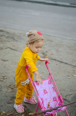 Photo of a toddler girl in the funny hat playing with a toy strollerの写真素材